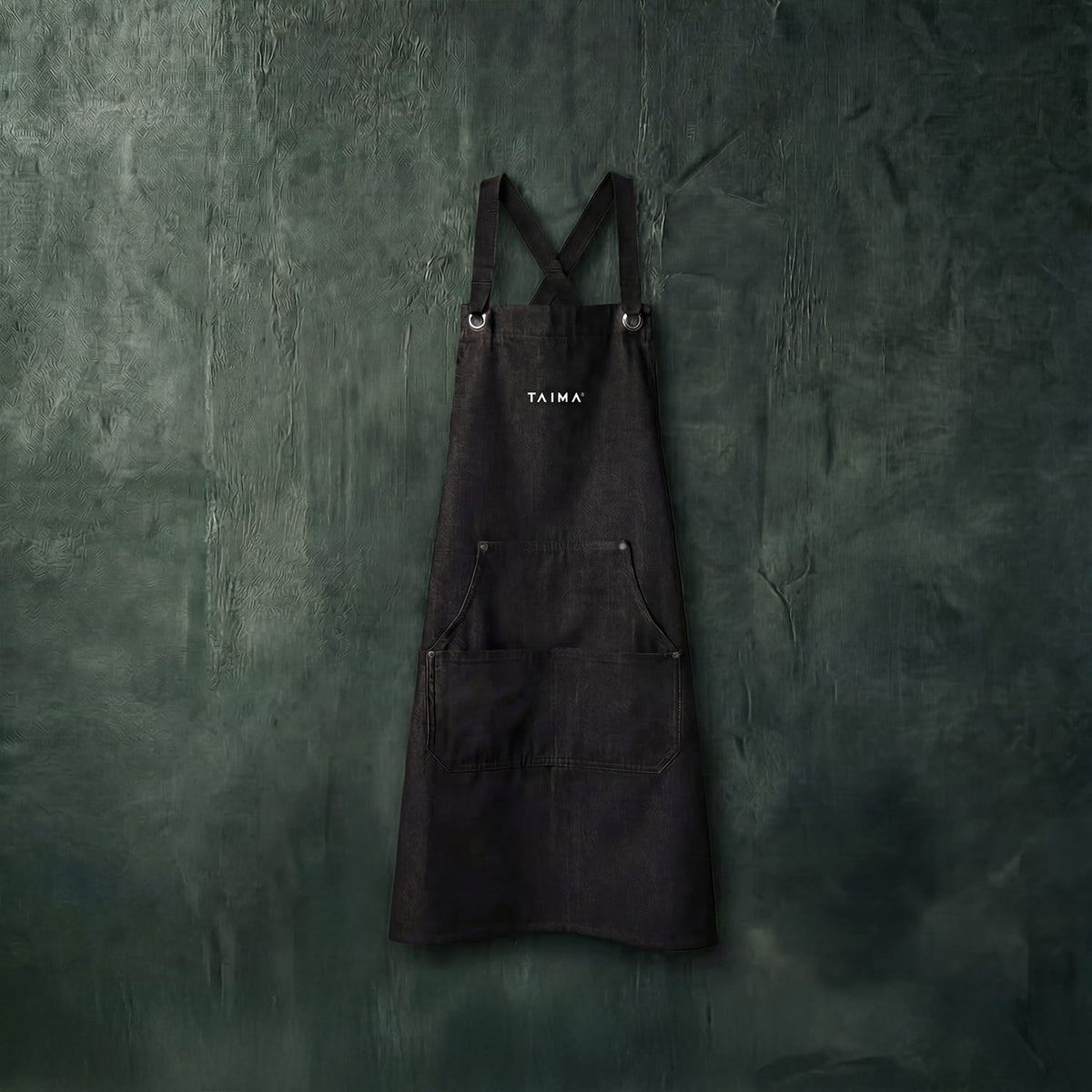 Black apron with 'Taima' branding on a textured green wall