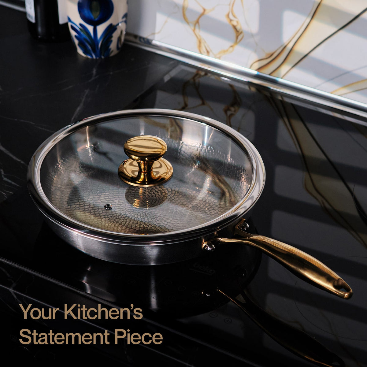 Titanium frying pan with gold handle and lid knob on a black stovetop.