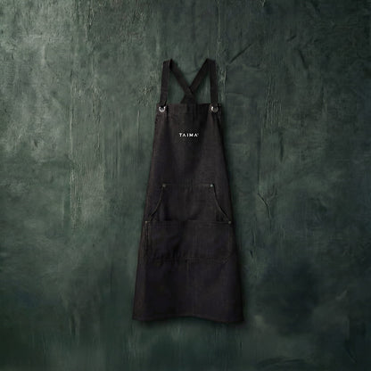 Black apron with 'Taima' branding on a textured green wall