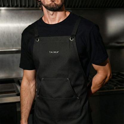 Person wearing a black apron with 'TAIMA' branding in a kitchen setting