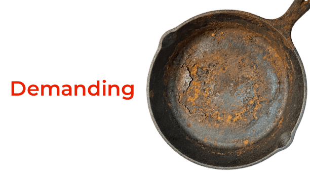 Rust-covered cast iron skillet with the word 'Demanding' in red text on a black background