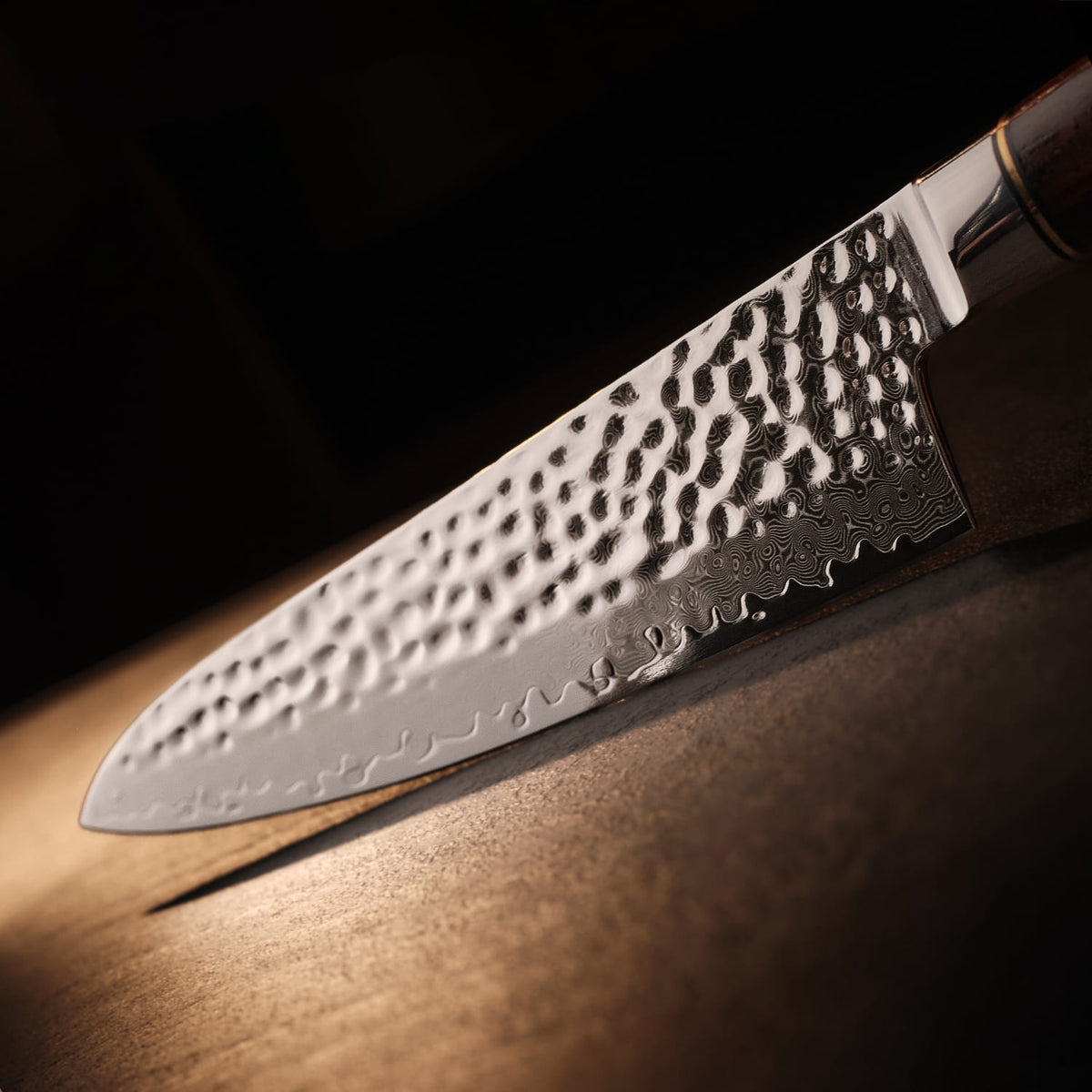 Hammered stainless steel kitchen knife on a wooden surface with a dark background