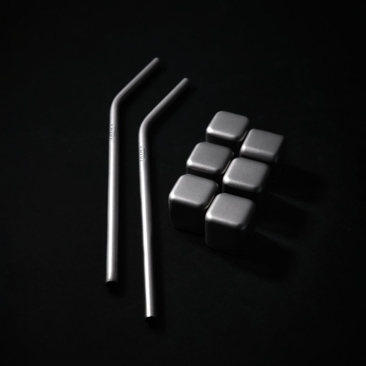 Two metal straws and six metallic dice cubes on a black background