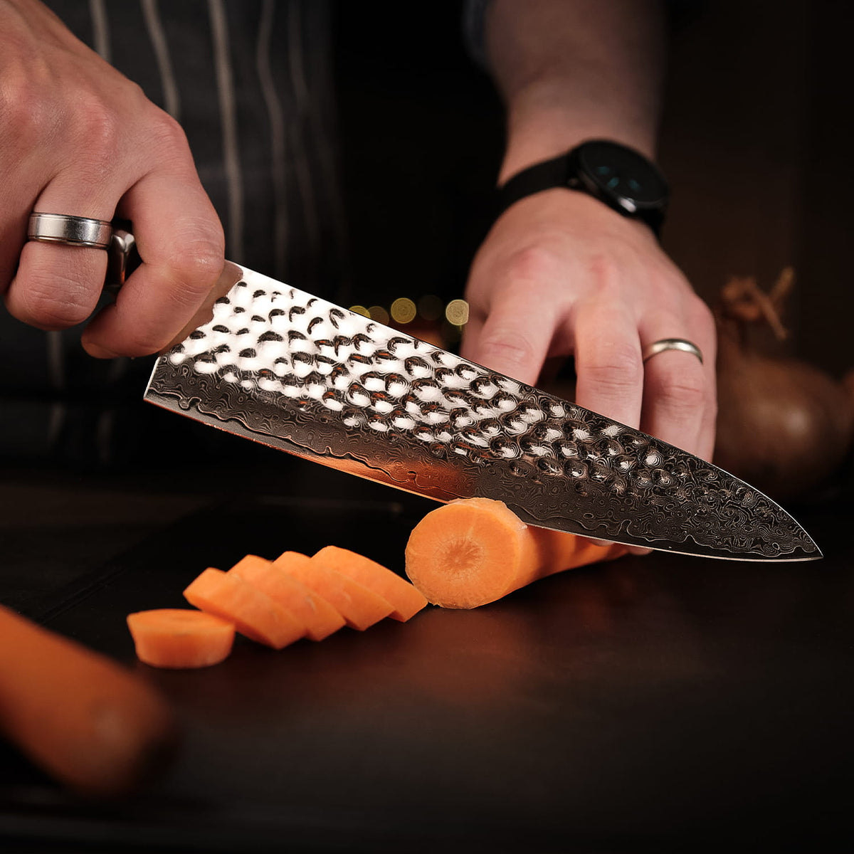 Person using a chef's knife to slice carrots on a dark surface