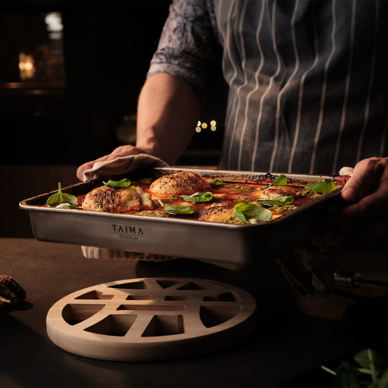 Person holding a titanium tray of food with Taima branding in a dimly lit setting