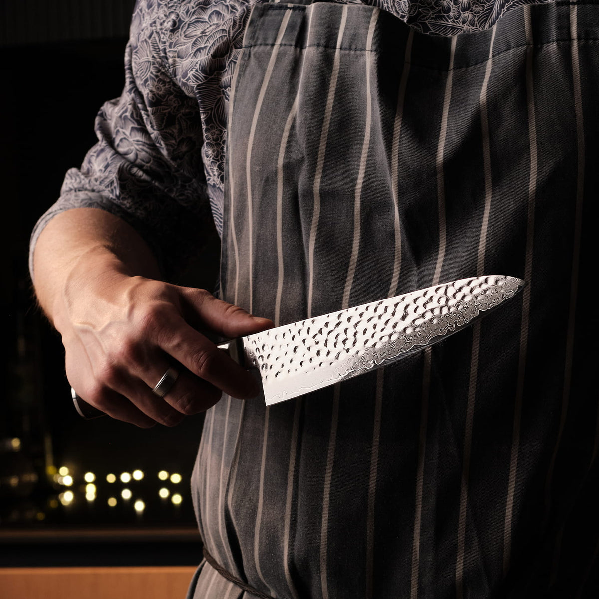 Person wearing a striped apron holding a chef's knife