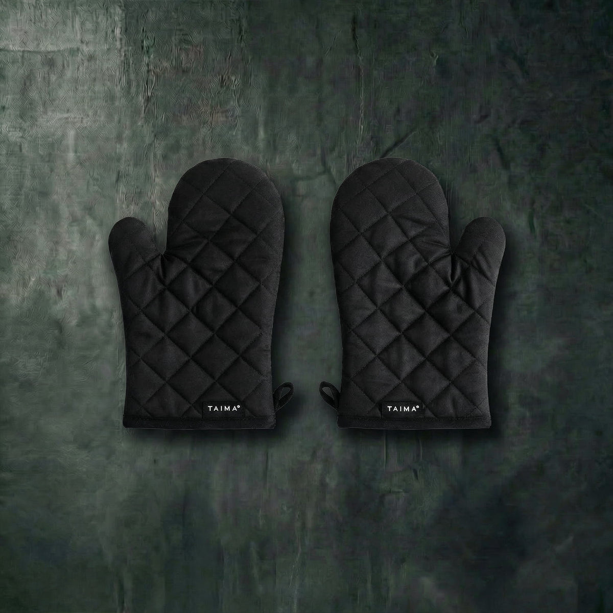 Pair of black quilted oven mitts on a dark textured surface