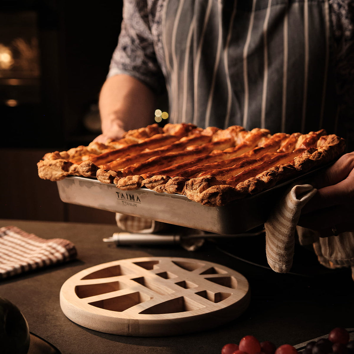 Person holding a tray with a baked dish, likely a pie, in a kitchen setting.