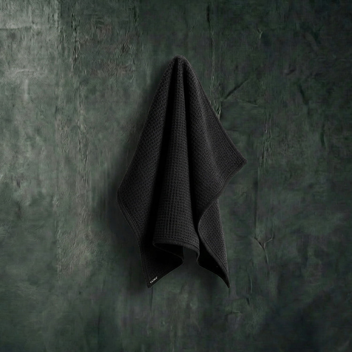Dark gray towel hanging on a textured green wall
