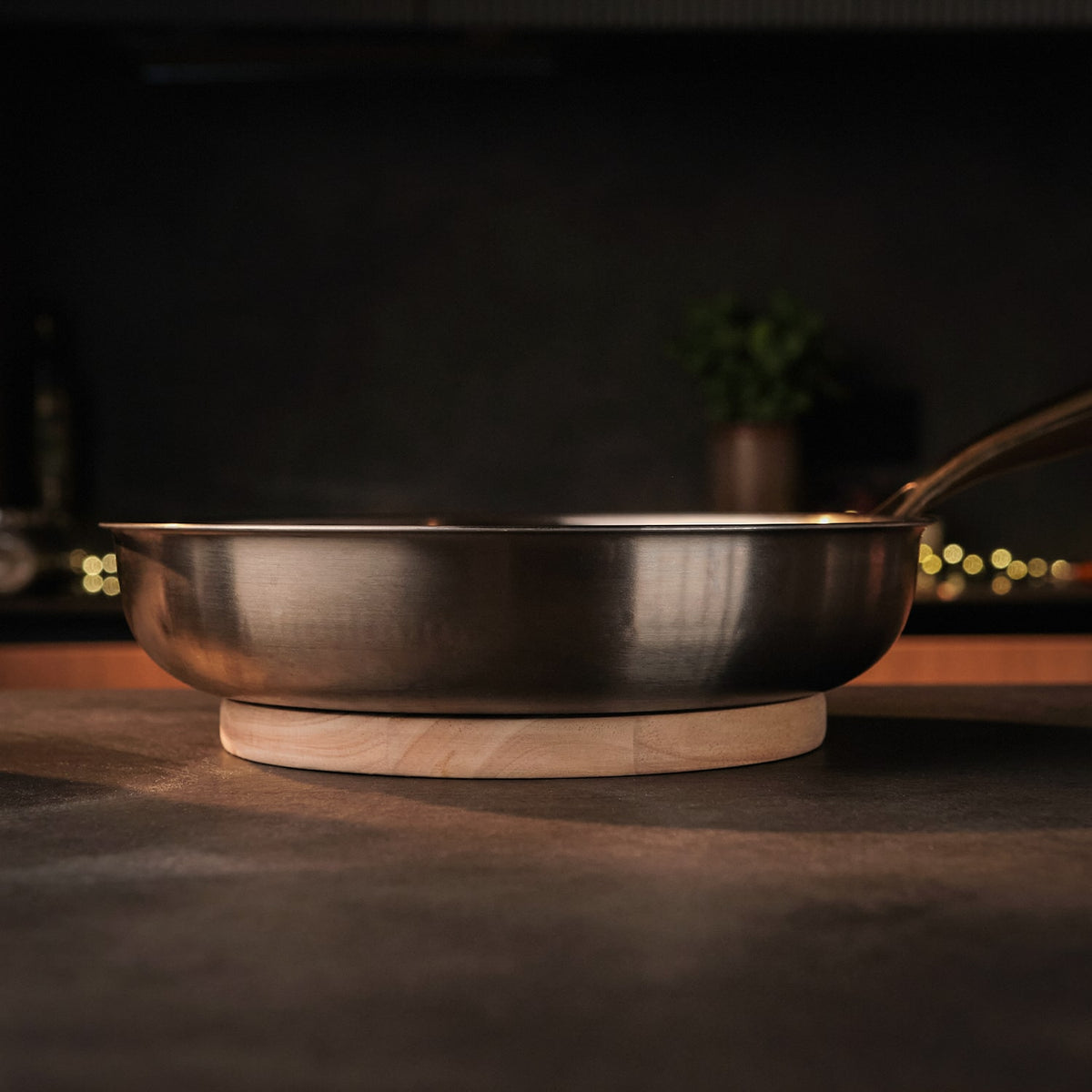 Titanium steel frying pan on a wooden trivet with a blurred kitchen background